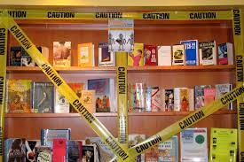 Caution tape over a bookshelf to show the way that certain books are being viewed. 